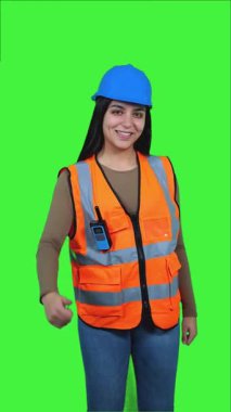 dikey özgüvenli Latin inşaat işçisi kadın güvenlik yeleği giyiyor ve yeşil ekran arka planına başparmak işareti yapıyor, profesyonel onay ve başarıyı ifade ediyor