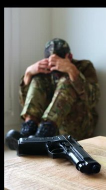Dikey asker kamuflaj üniforması duvarın yanında, elinde silahla oturuyor, ellerinde yüzünü saklıyor, travma sonrası stres bozukluğu yaşıyor, umutsuzluk ve depresyon belirtileri gösteriyor.