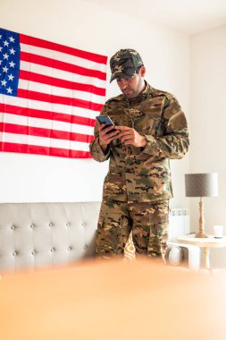 Akıllı telefon kullanarak ve kulaklıkla müzik dinleyerek travma sonrası stres bozukluğundan duyduğu üzüntüyü dile getiren, kamuflaj üniformalı dikey Amerikan askeri.