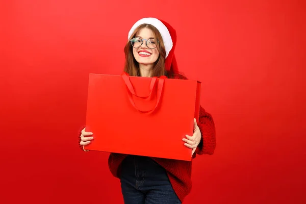 Positive woman in santa hat with red bag in her hands, christmas discounts. Buy and give Christmas gifts.