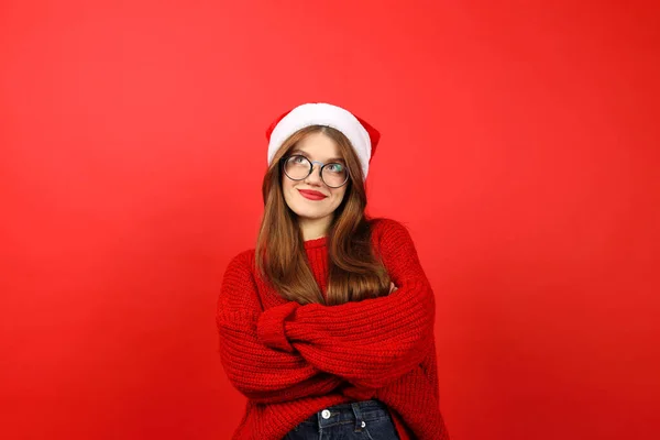 赤いお正月のセーターを着た女の子とサンタの帽子が決定します クリスマスへの贈り物を選ぶことを考えてみてください — ストック写真