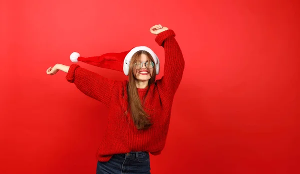 Happy dancing girl in headphones and Christmas clothes on a red background. Fun holiday playlist.