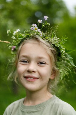 Çiçekli bitkisel çelenk içinde gülümseyen küçük kız, yakın plan portresi..