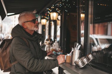Kıdemli adam caddedeki küçük bir kahve dükkanında içki ısmarlar. Sokak perakendecisi, fast food.
