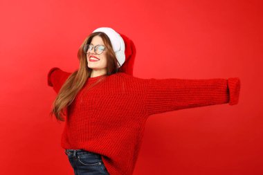 Kulaklıklı ve kırmızı arka planda Noel Baba şapkalı mutlu bir kadın dans ediyor, müzikten zevk alıyor. Yeni yıl partisi..