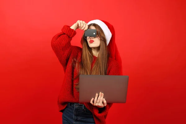 Online shopper. Attractive woman with credit card and laptop wearing santa hat on red background.
