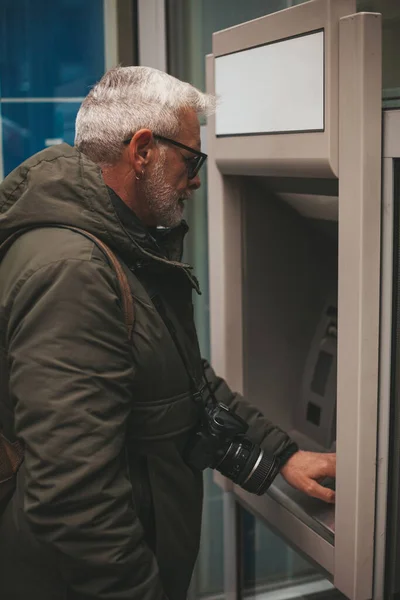 An elderly man withdraws cash from an ATM. Takes savings in a panic.