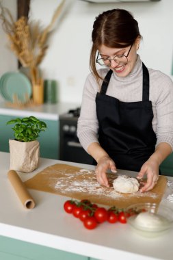 Kadın aşçı klasik margarita pizzası hazırlar. Gülümseyen ve hamuru yoğuran.