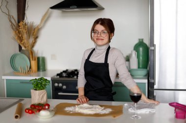 Mutfakta bir bardak şarapla klasik bir pizza hazırlayan genç bir kadının portresi..