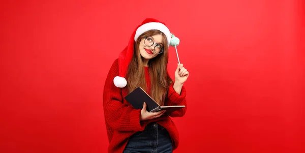 Wishes for Christmas. To do list and gifts in the hands of a cute girl on a red background.