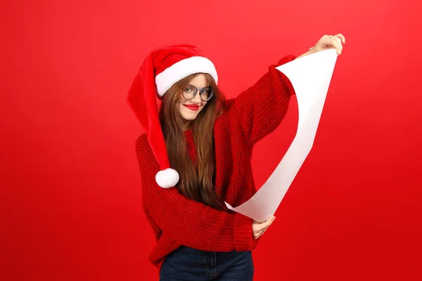 Wish list for Santa Claus in the hands of a young woman on a red background. Christmas wishes.