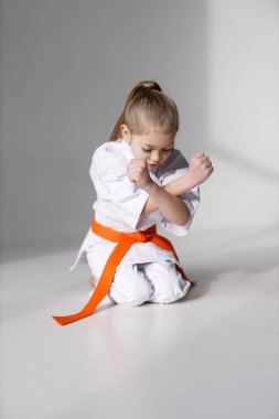 A small child is a karate student, sitting position on a white background.