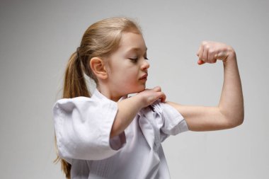 Little strong girl shows her biceps, karate training.