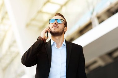Young guy in glasses and suit talking on the phone and looking up.
