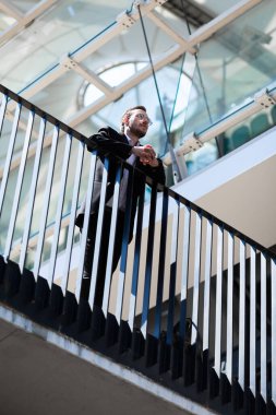 Businessman stands on balcony in thought, focused.