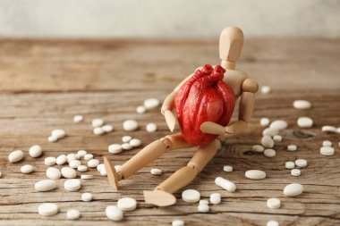 Oyuncak adam elinde anatomik bir kalp tutuyor, hapların yanına oturuyor. Kardiyovasküler sistem tedavisi, kalp krizi önleme.