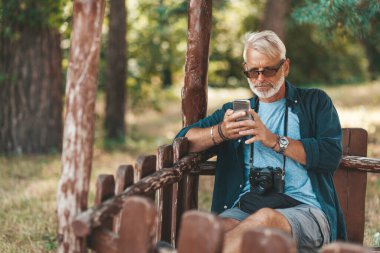 An attentive and focused senior citizen uses a cell phone. Use of online social networks and banking services in old age.