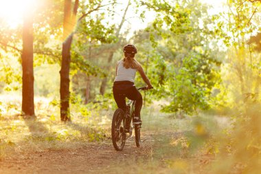 A woman rides a bicycle along a path in the forest at dawn. Cardio and healthy lifestyle.