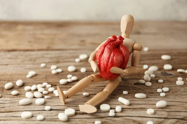 Toy man holds an anatomical heart in his hands, sits next to pills. Cardiovascular system treatment, heart attack prevention.