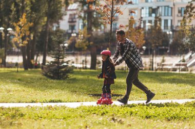 Dad and daughter roller-skate in the park. Leisure weekend together.