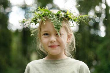 Smiling girl in a wreath of flowers and plants, unity with nature.