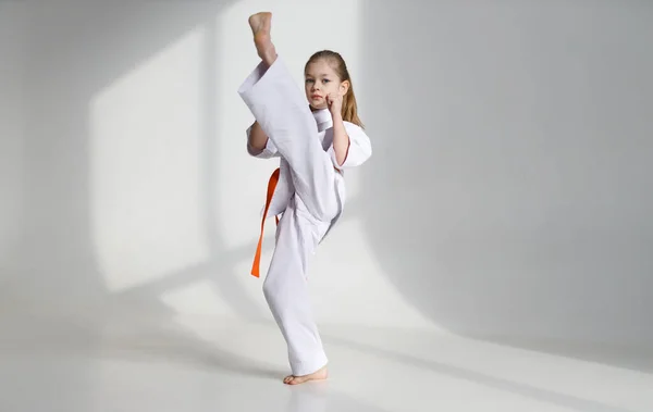 Karate kick, little girl in a kimono on a white background, training.