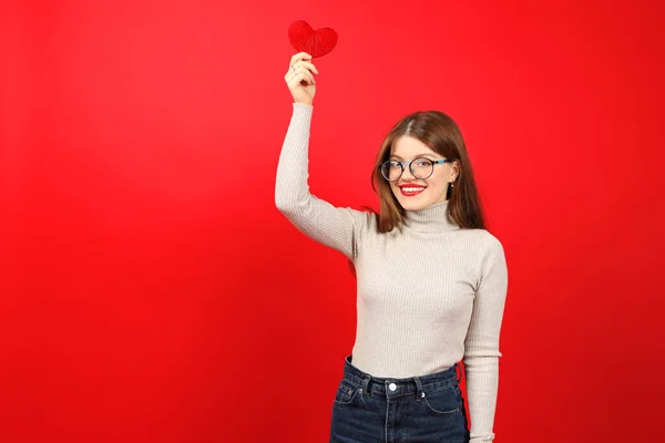 Young female volunteer with a heart in her hands on a red background.