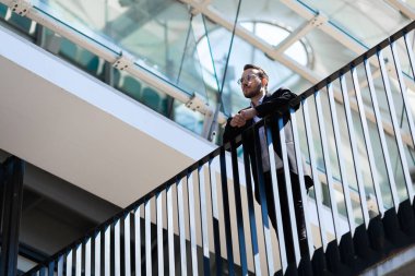 Businessman stands on balcony in thought, focused.