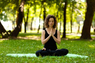 Kadın sabahları parkta temiz havada yoga yapıyor. Lotus pozu.