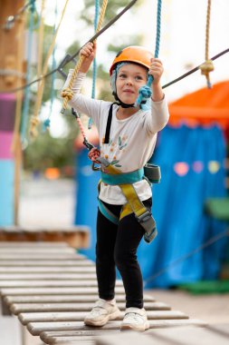 Miğferli küçük kız dışarıdaki macera parkında iplere tırmanıyor. Olağanüstü spor, doğada aktif eğlence..
