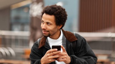 Gülümseyen Afrikalı Amerikalı adam telefonda arkadaşlarına SMS yazıyor..