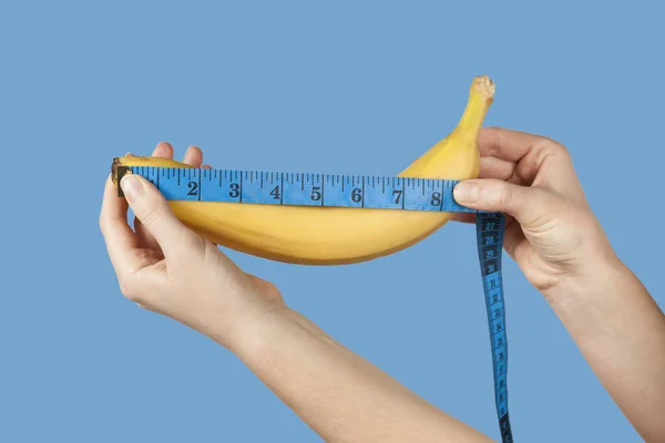Measuring the size of a banana as a symbol of the male penis isolated on blue background. Big dick length. Strong erection and impotence problem.