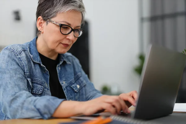 stock image Senior woman in glasses works on a laptop.