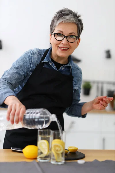 Felice Donna Anziana Casa Interno Versa Acqua Bicchieri Con Limone — Foto Stock