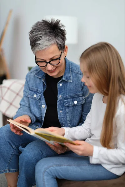 stock image Happy child reads a book with his grandmother in the home interior.