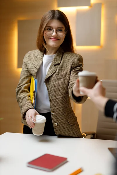 stock image Employees in the office on a coffee break. Young smiling woman is sharing a hot drink with a colleague, vertically.