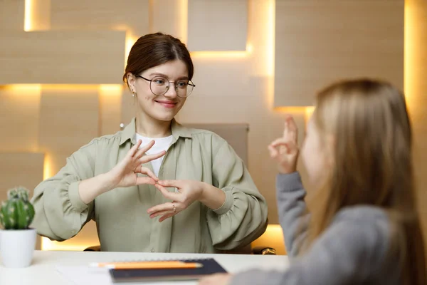 Learning sign language, cheerful woman communicates with a child. School for the deaf or dumb.