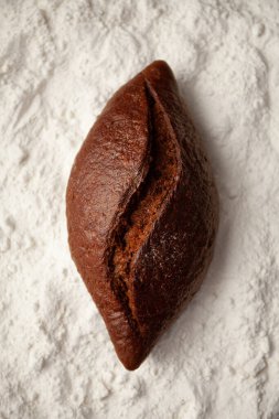 Beyaz undan bir zemin üzerinde siyah ekmek. Tam tahıllı ekmek..