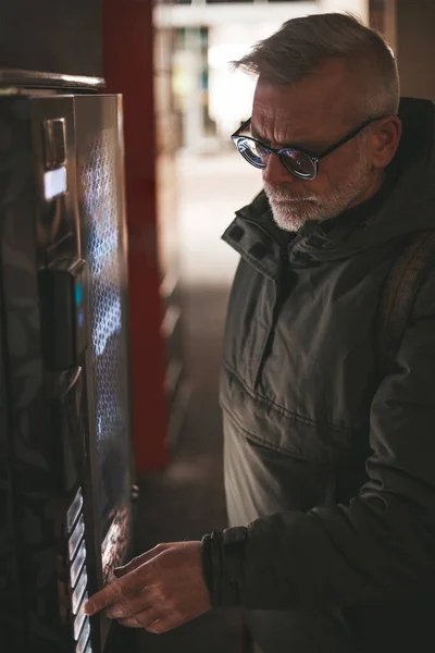 Mature man buys a drink from a vending machine. Hot coffee outside, automatic retail.