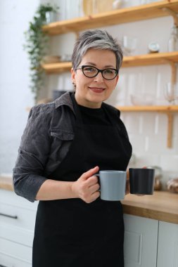 Mutfakta elinde fincanlarla yaşlı bir kadının portresi, pozitif sabah havası..