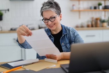 Gözlüklü, gülümseyen, iç mekandaki mektuplara bakan son sınıf öğrencisi..