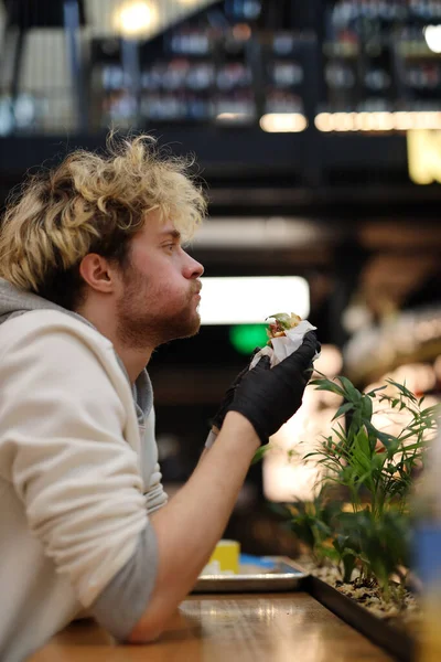 Jeune Homme Aux Cheveux Bouclés Déguste Délicieux Hamburger Dans Café — Photo
