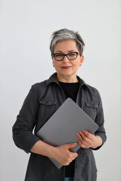 stock image Portrait of a mature woman with a laptop in her hands on a gray background, vertically.