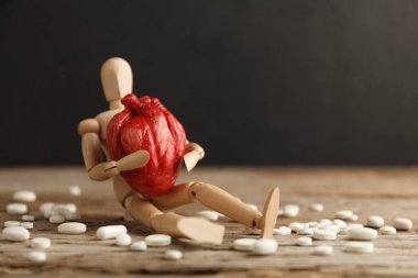 Oyuncak adam elinde anatomik bir kalp tutuyor, hapların yanına oturuyor. Kardiyovasküler sistem tedavisi, kalp krizi önleme.
