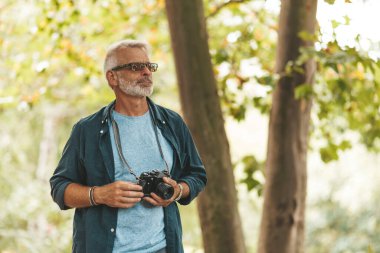 Dışarıda sakallı yaşlı bir adamın aktif hobisi. Bir emekli seyahat ederken kamerayla doğanın fotoğraflarını çeker..