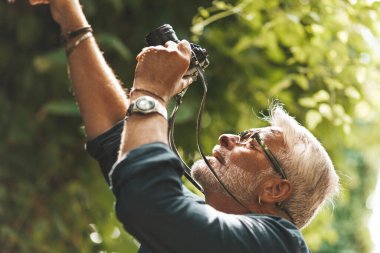 Meraklı yaşlı bir adam ormanda bitkilerin fotoğraflarını çekiyor. Emekli turist doğayı keşfediyor..