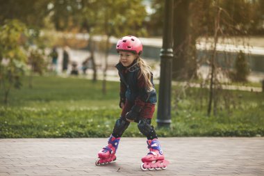 Küçük tatlı bir kız buz gibi sonbahar havasında parkta paten kayıyor..