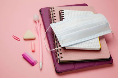 Pembe arka plan üzerinde çalışmak için yüz maskesi ve kırtasiye malzemesi. Karantina kısıtlamaları, korunma ve hastalıkların önlenmesi. Bir salgın sırasında çalış.