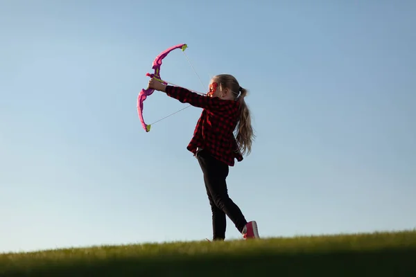 stock image Little girl shoots a bow on the background of the horizon. Imaginary archer game, superhero in dreams.