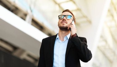 Young guy in glasses and suit talking on the phone and looking up.